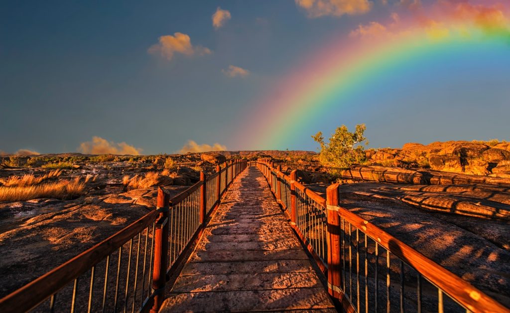 a path through a desert with a rainbow in a a blue sky