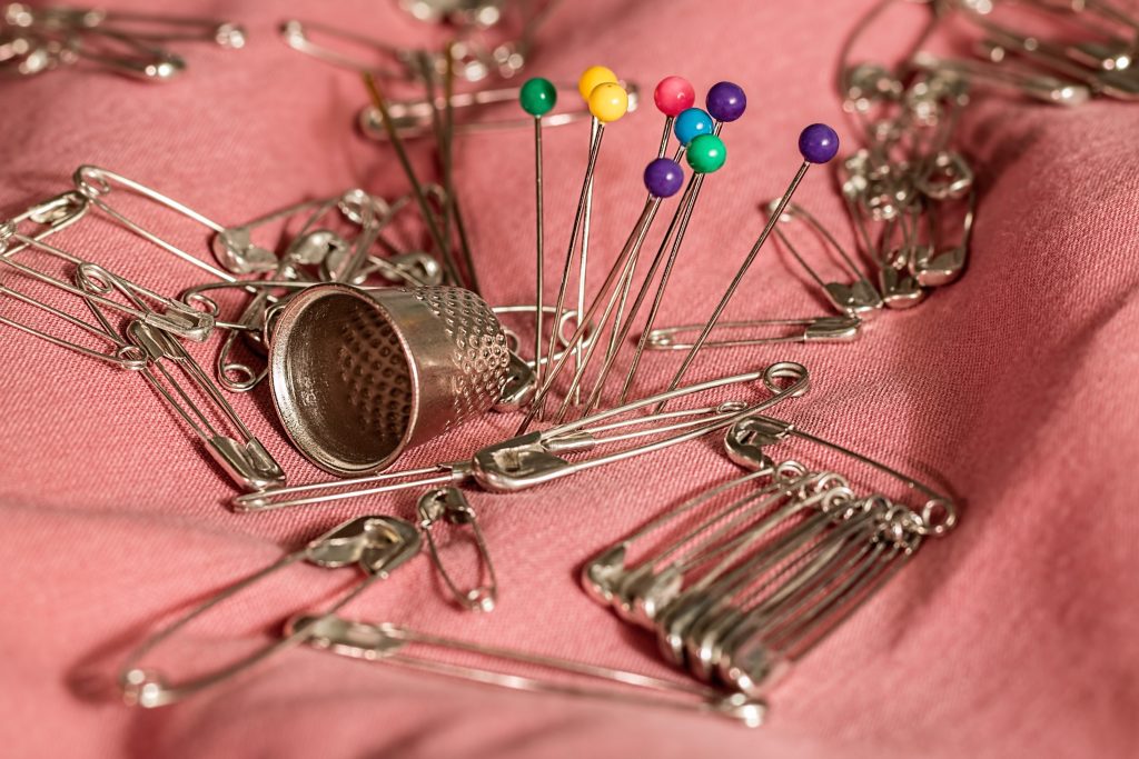 pins, safety pins and a thimble laid out on a swathe of pink cotton fabric