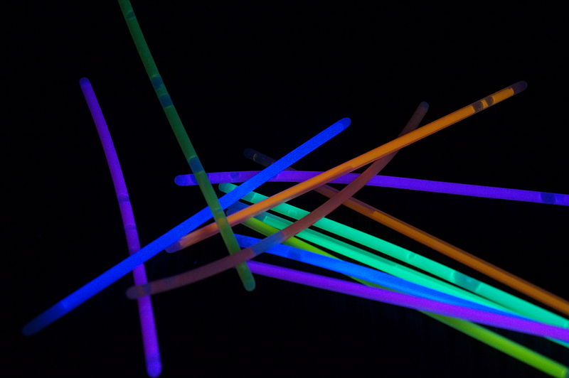 On a black background, a heap of different coloured glow sticks - activated and glowing: blue, orange, purple and green